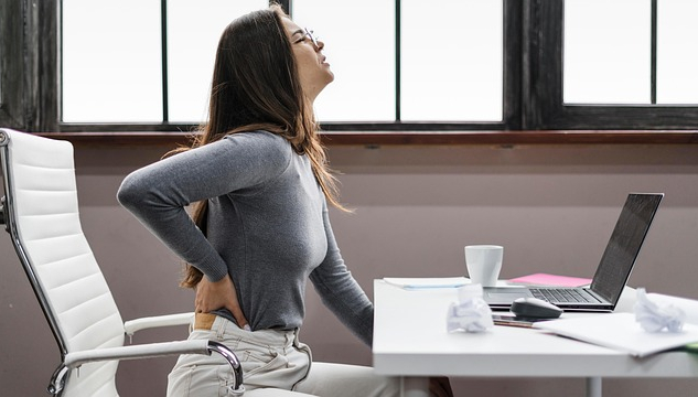 Woman sitting at a computer with her hand on her aching back.&nbsp;Image by fairpharma from Pixabay.&nbsp;